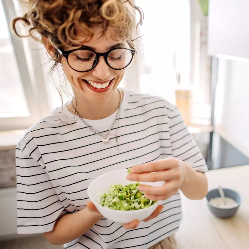 A Woman Smiles as She Mixes a Bowl of Greens