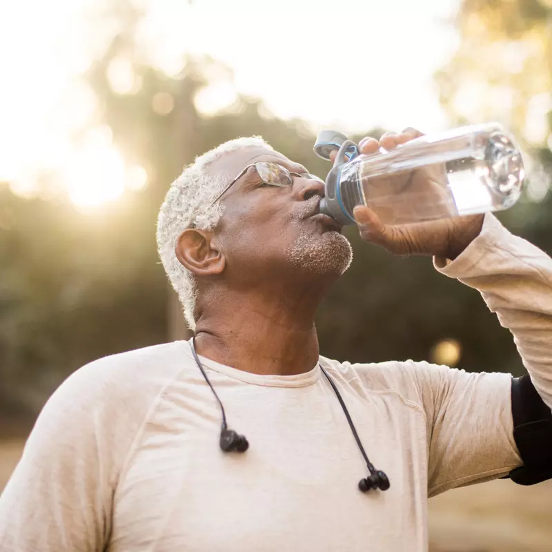 A Senior Man Drinks Water from a Reusable Water Bottle During a Break From His Run.