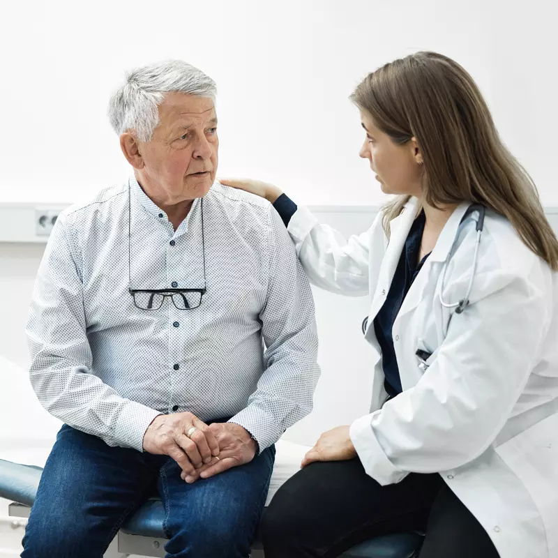 A Doctor Speaks Comfortingly With Her Senior Patient in an Exam Room 