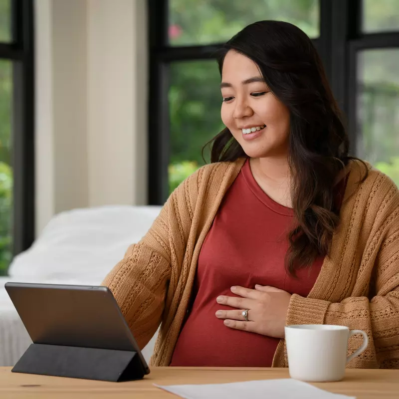 A Pregnant Woman Smiles as She Uses a Tablet at Home