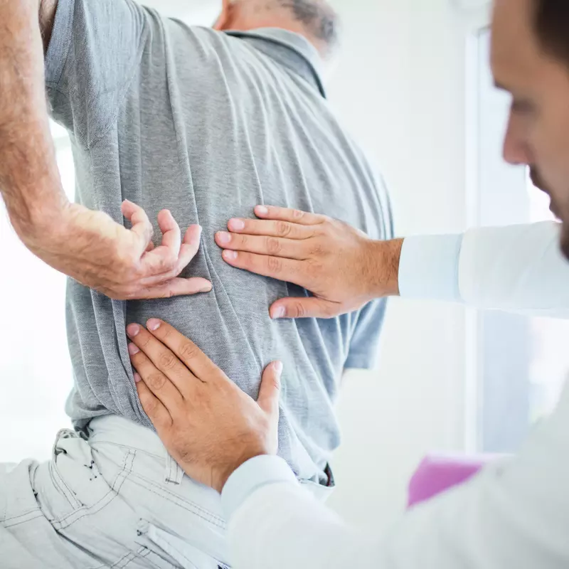 A Senior Patient Points Out to His Doctor where on His Back the Pain is