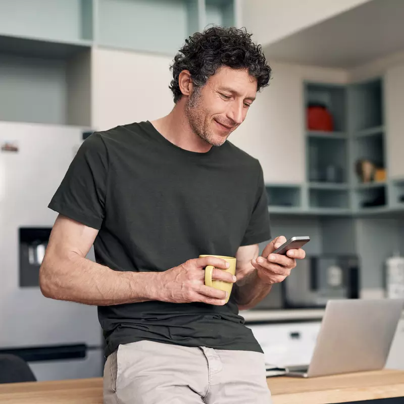 A Man Checks His Phone While Drinking His Cup of Coffee in a Kitchen
