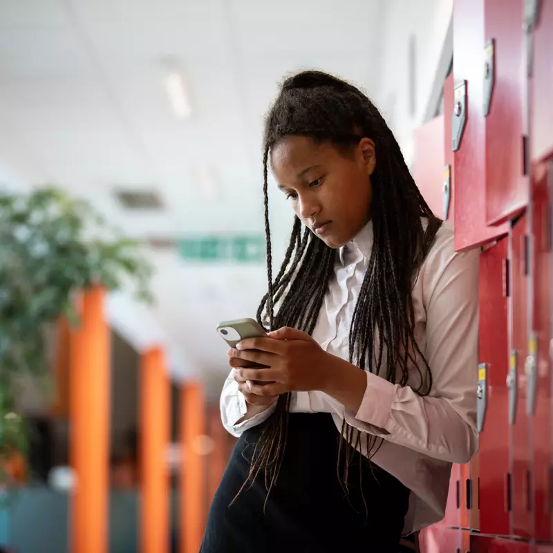 A Teenager Looks at Her Phone While Leaning Against Her Locker.