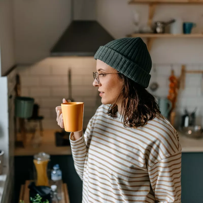 A Woman Enjoys a Hot Beverage While Looking Out the Kitchen Window During the Winter