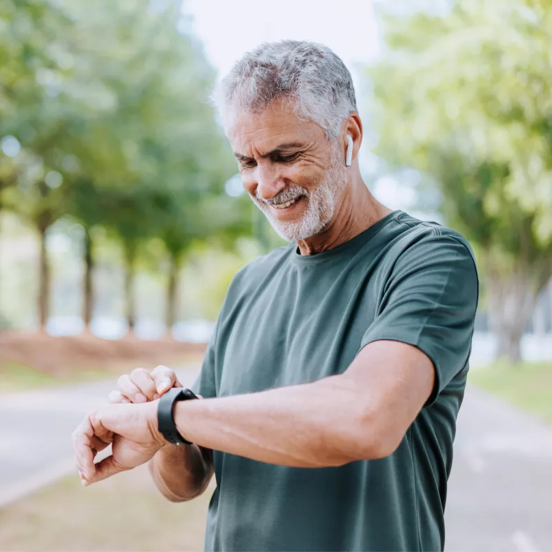 A Senior Man Checks His Smart Watch as he Takes a Break from His Walk