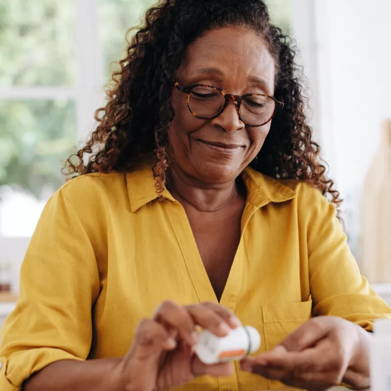 A Woman Sits at the Kitchen Table and Shakes a Pill Out of a Bottle