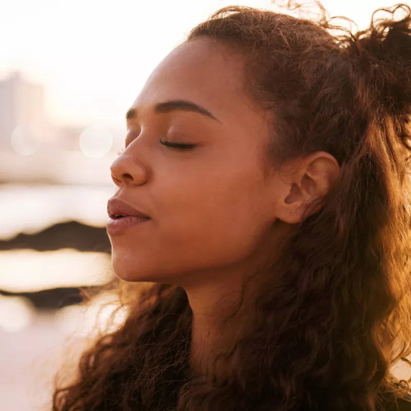 A Woman Stands Outside with Her Eyes Closed, Concentrating on Her Breathing