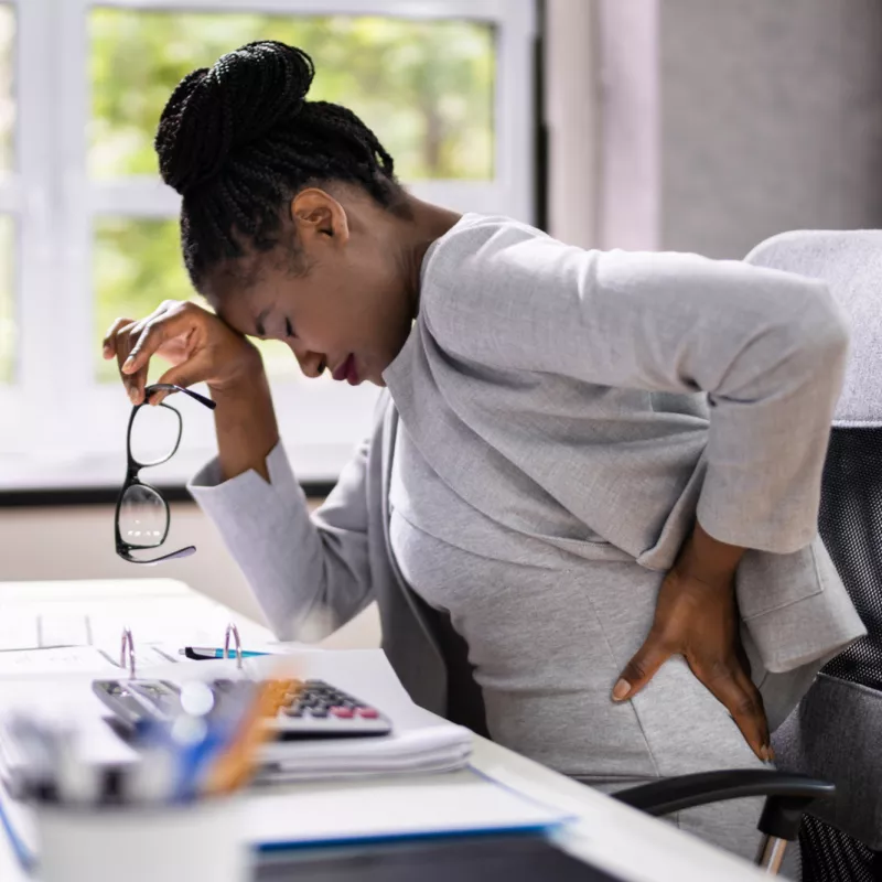 A Woman Sitting at Computer Leans Forward Because of Back Pain