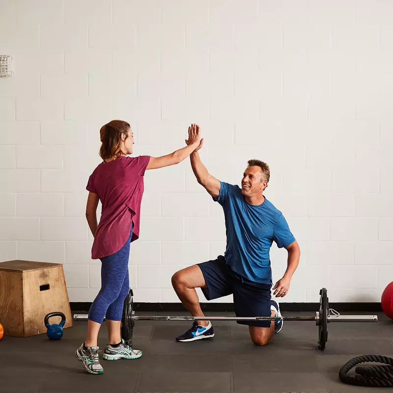 A Caucasian man and woman high-five while exercising at the gym.