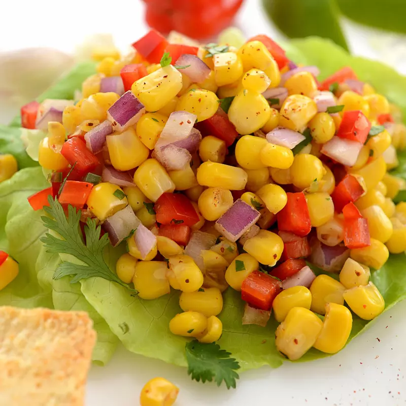 Corn with diced red pepper and red onion salsa on a bed of lettuce