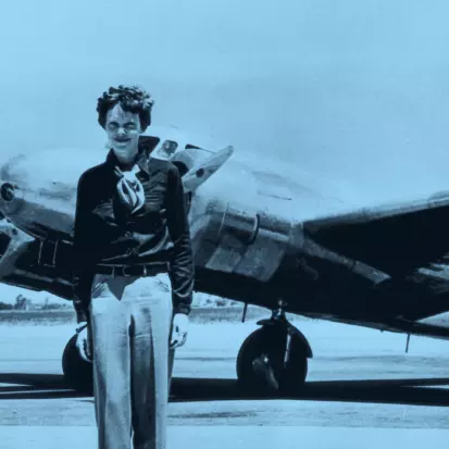 Amelia Earhart standing in from of a plane