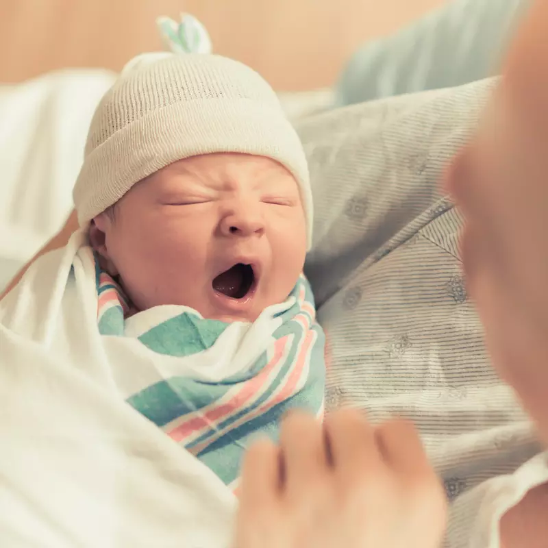 Newborn baby yawning in it's mother's arms