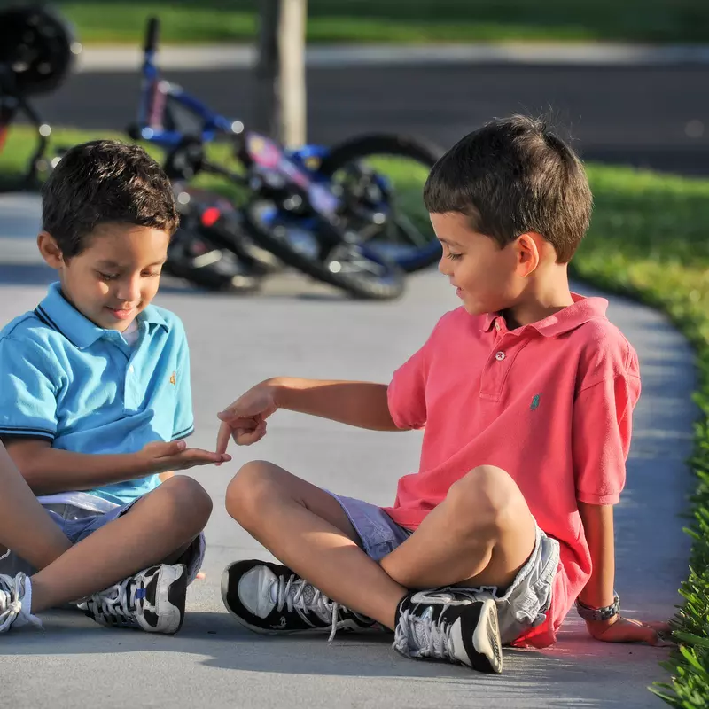 Two young boys sitting and playing outside.