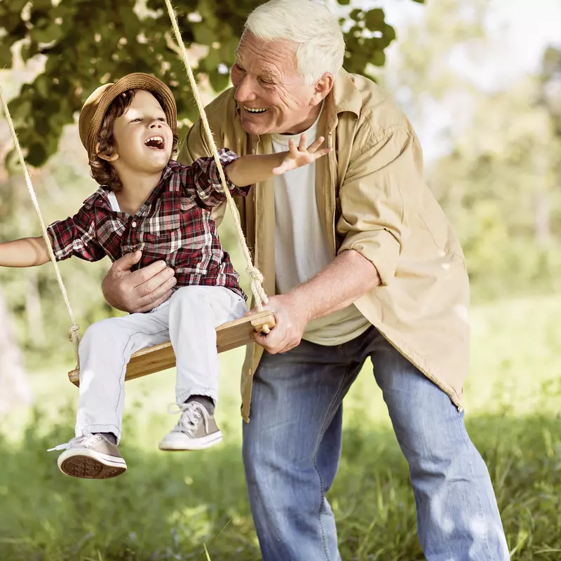 Grandfather pushes grandson on a tree swing