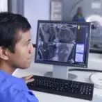 A male radiologist studies CT scan images on a computer.