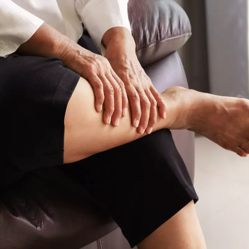 A person sitting down massaging their calf due to pain.