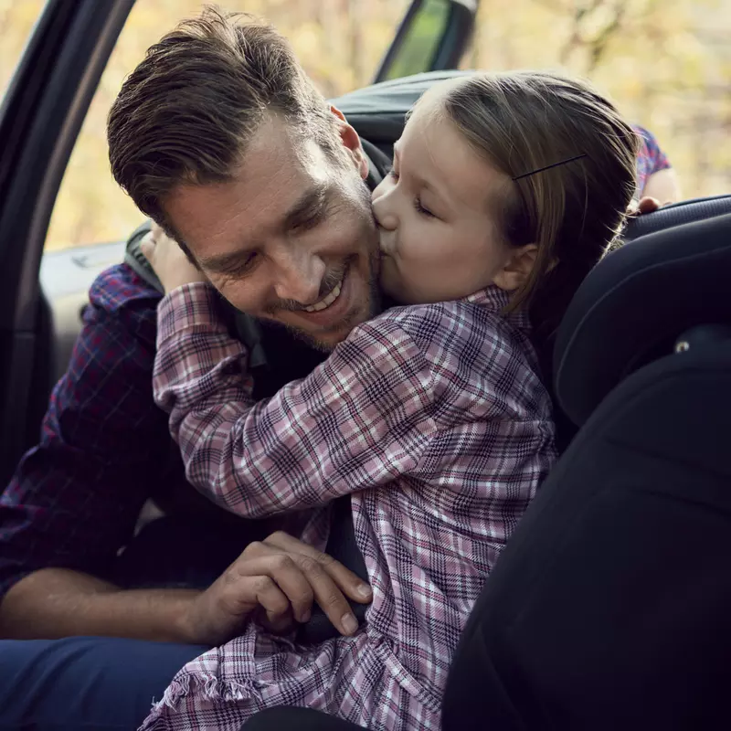 A dad buckles his daughter into a carseat in the backseat of a car.