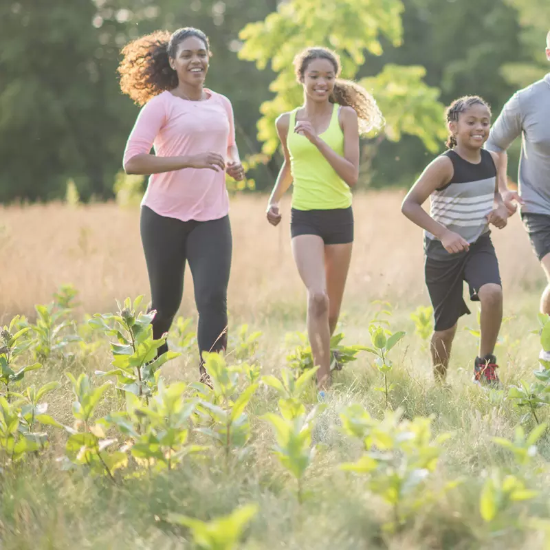 A family of four, running together outside in a field.