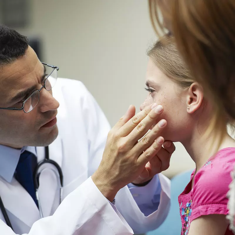 A male doctor examines the eyes of a young girl.