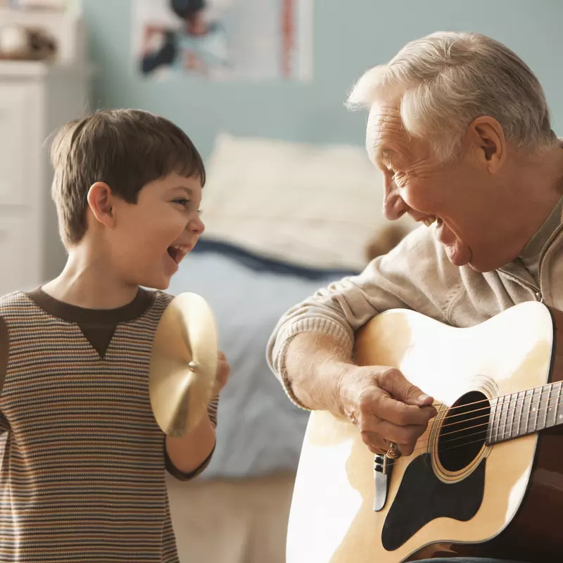 Grandfather playing guitar for grandson while grandson plays the cymbals