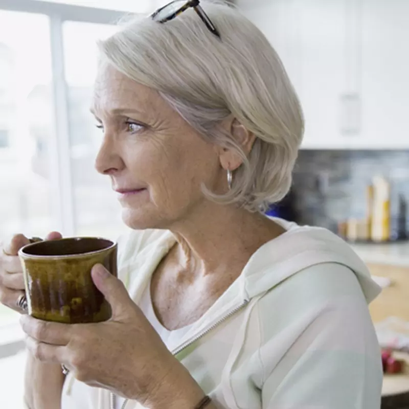 An adult Caucasian woman sips coffee from a mug.