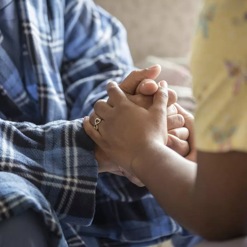 Close-up of a nurse and cancer patient holding hands.