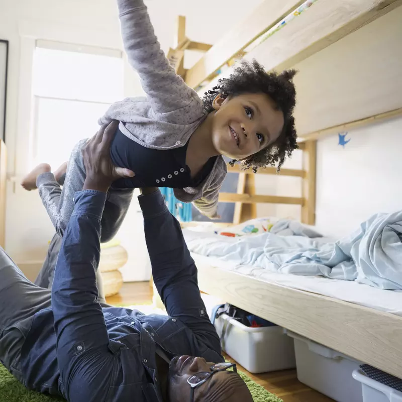 Father and child playing airplane in a kid's bedroom