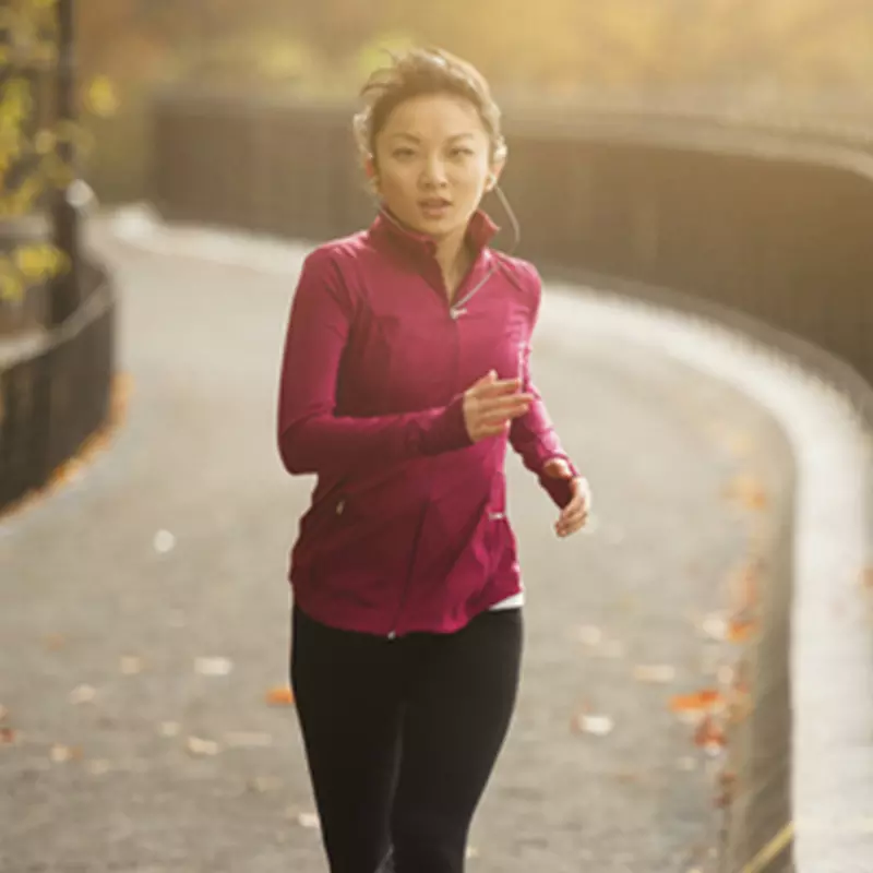 A young Asian woman jogs in the park on a fall afternoon.