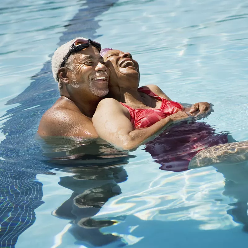 An adult African American couple swims in a pool on a hot day.