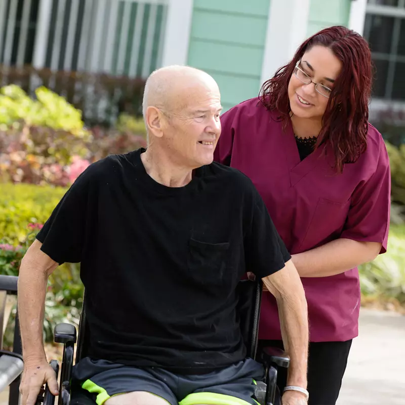 Elderly man in a wheelchair outside with a nurse.