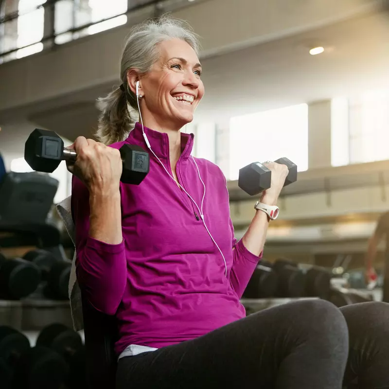 An elderly woman lifting weights at the gym.