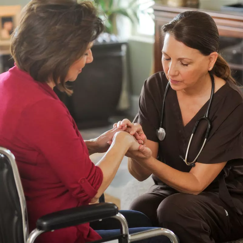 Woman in a wheelchair praying with a nurse.
