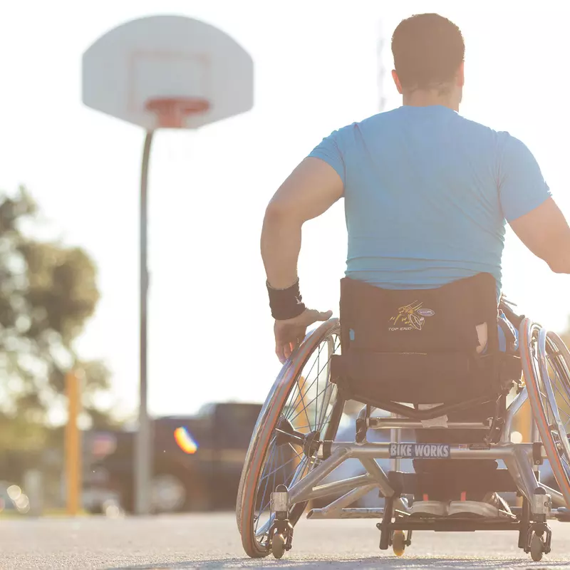 Man in a wheelchair playing basketball outside.