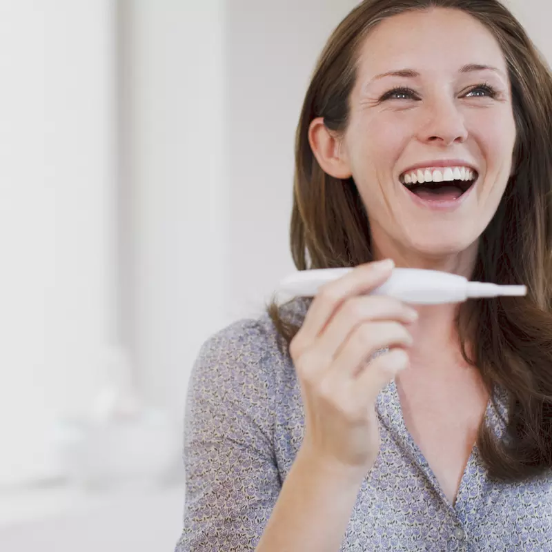 Happy woman laughs at the positive pregnancy test