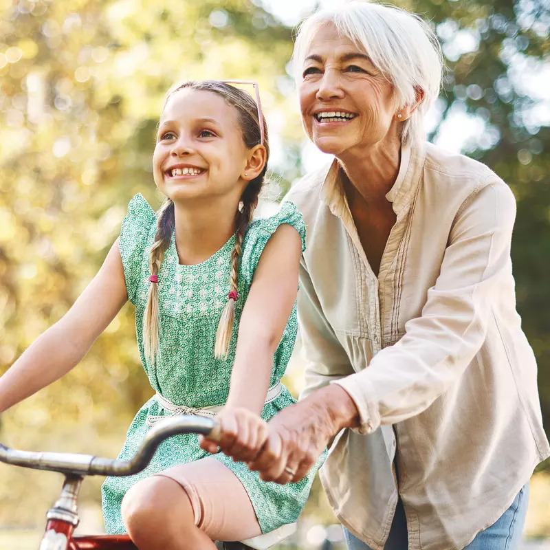 A grandmother helps her granddaughter ride a bike.