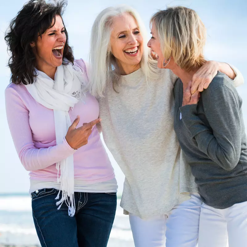 Three women laughing during a walk on the beach.