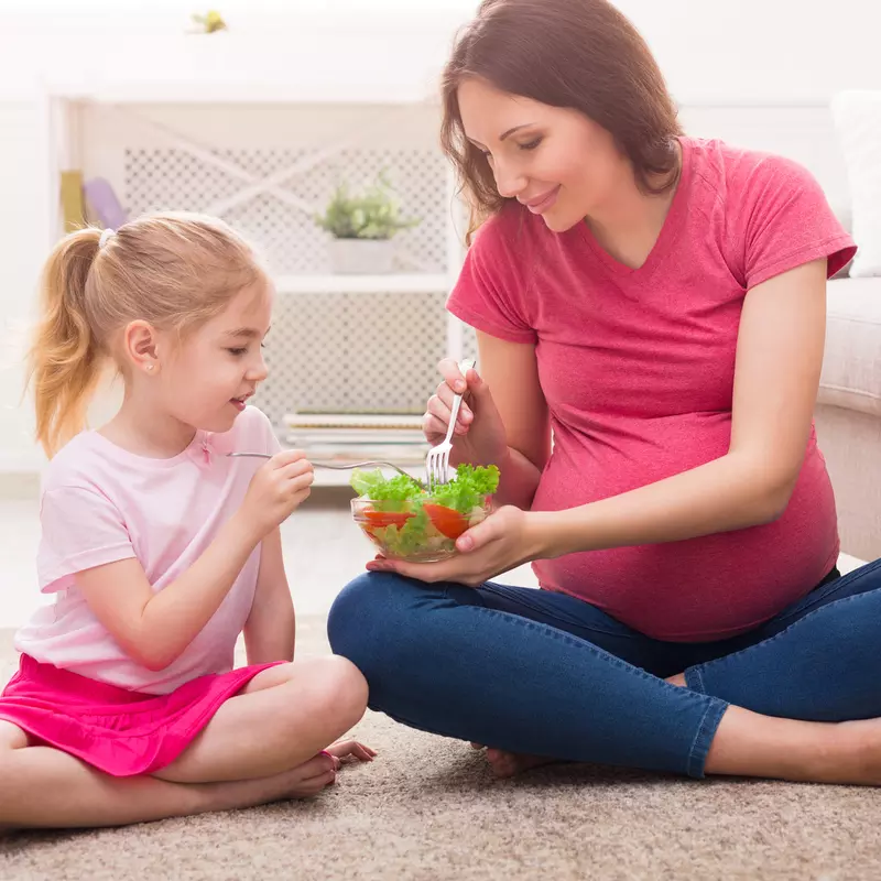 A pregnant mother teaching her daughter healthy eating habits