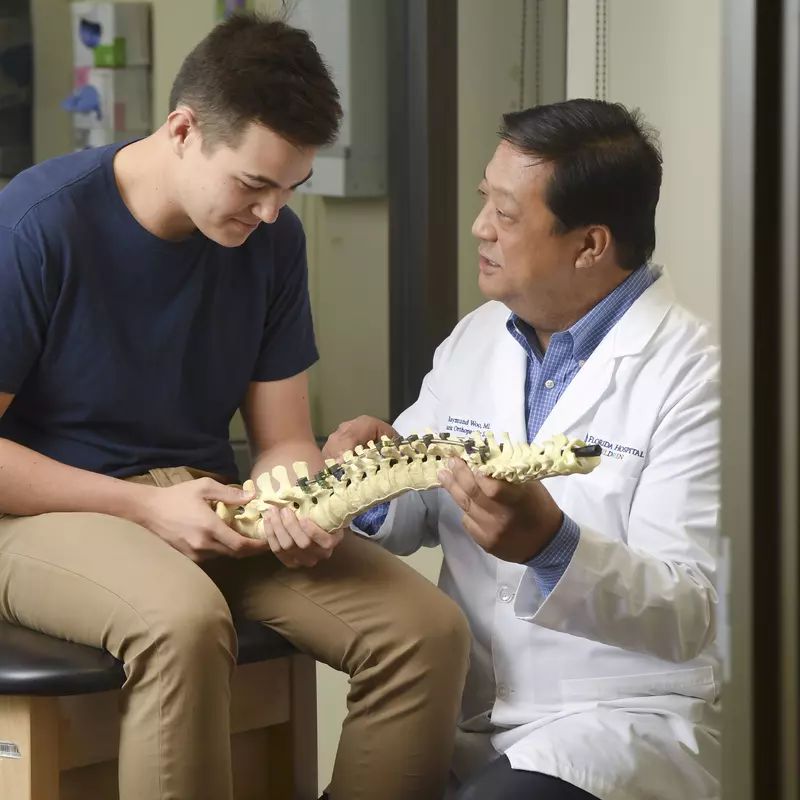 A doctor showing a spine skeleton to a young male patient.