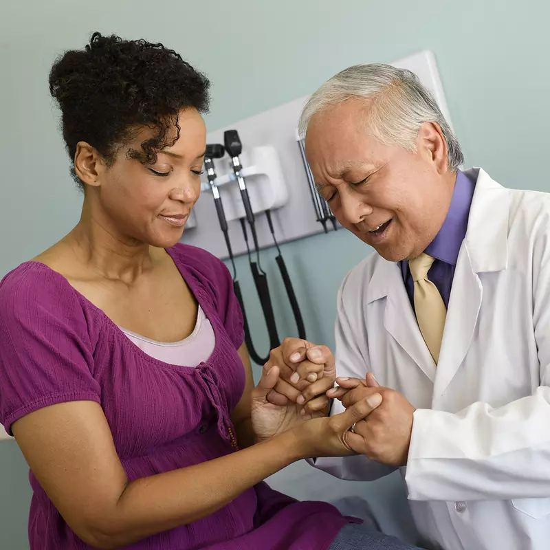 An Asian doctor prays with an African-American woman at the hospital.