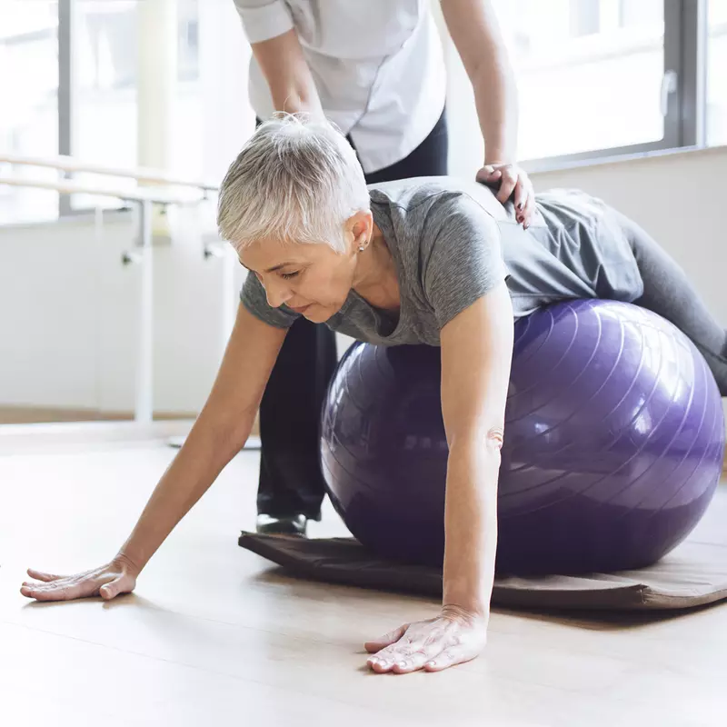 A Caucasian woman balances herself on an exercise ball.