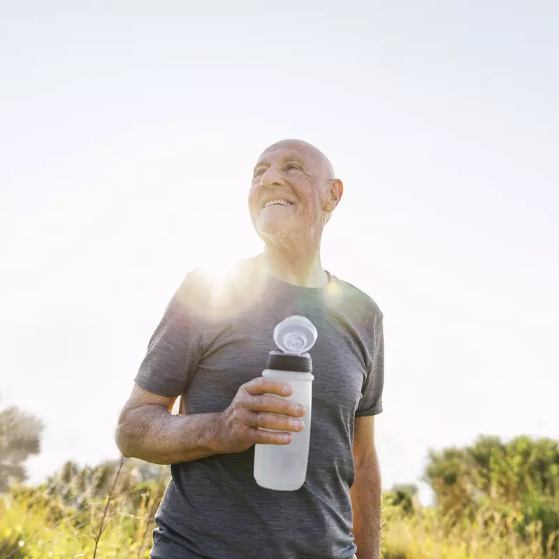 An older man takes a water break during a sunny outdoor hike