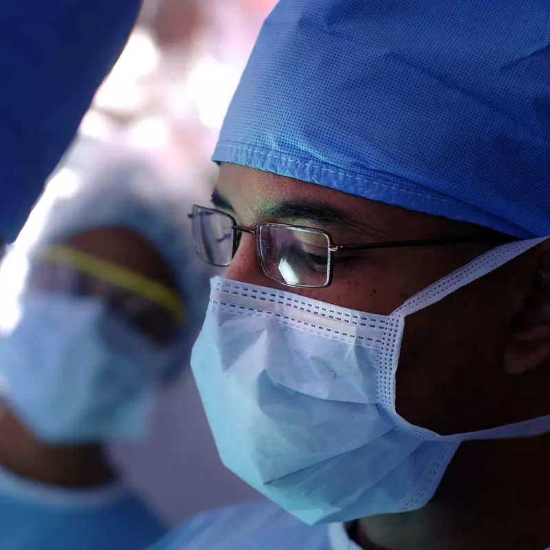 Male surgeon wearing glasses and a face mask.