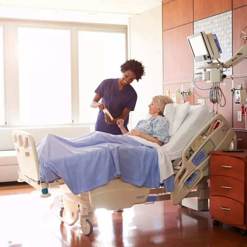 Nurse stands at the bedside of a woman in the hospital.