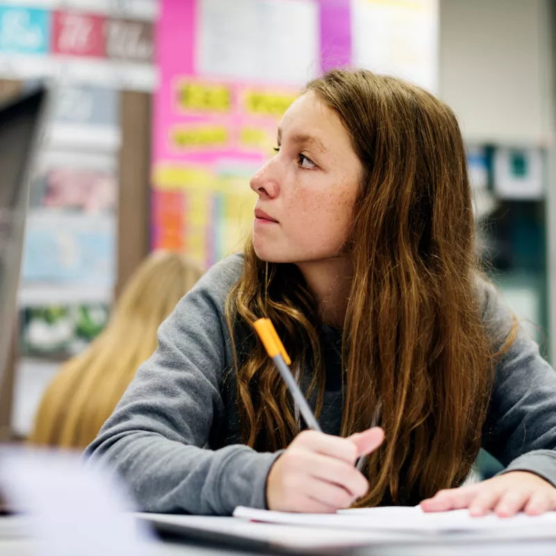 A Teen Student Sits in a Class Taking Notes