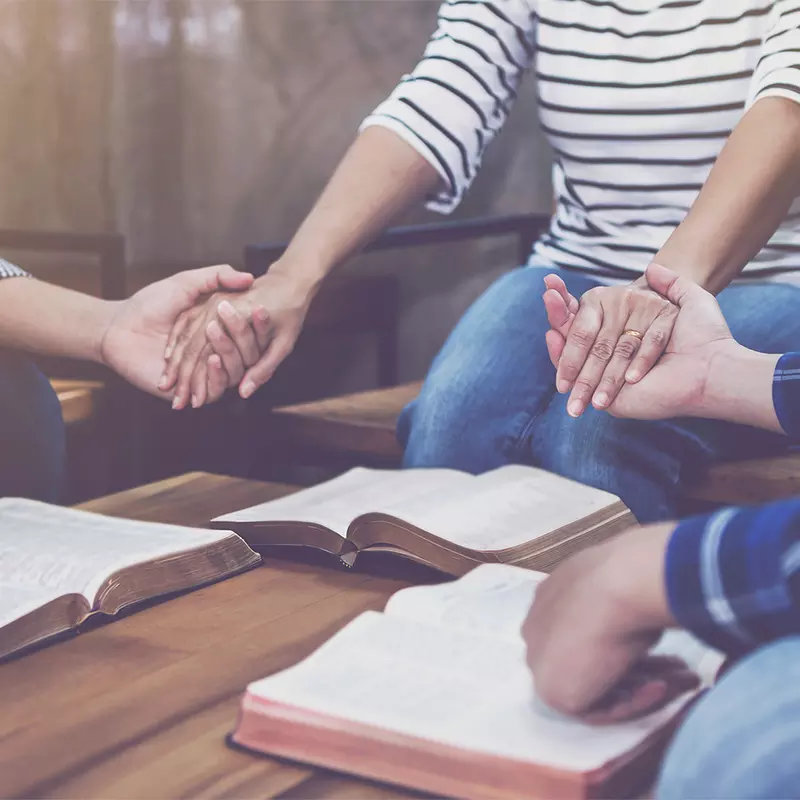 Adults holding hands in prayer at a Bible study.