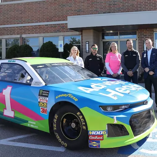 People standing next to the AdventHealth branded Nascar