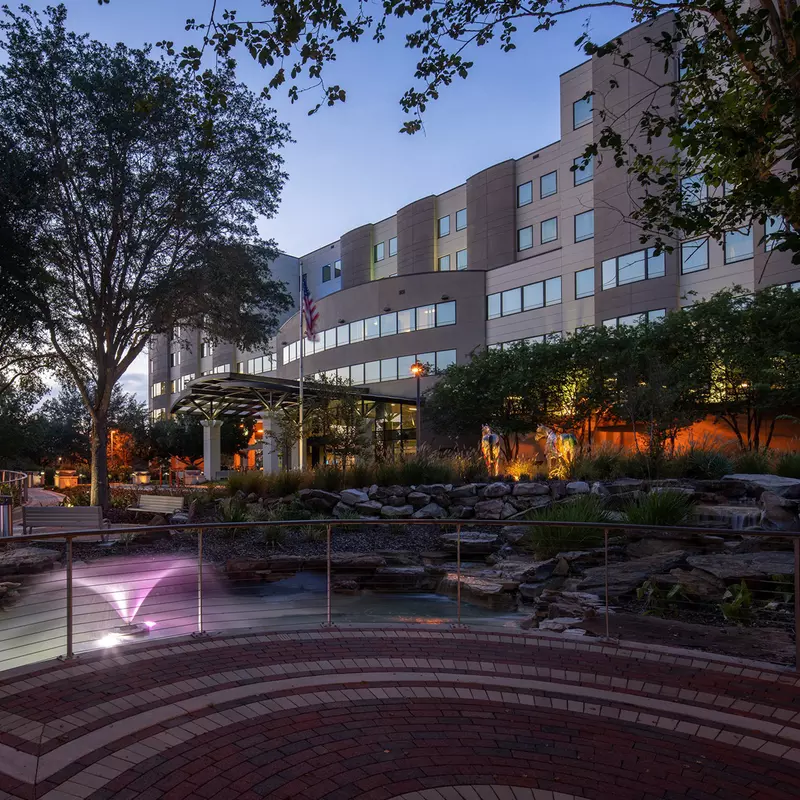 A photo of AdventHealth Ocala taken at dusk. A brick walking path with a railing is in the foreground and the hospital is in the background. 