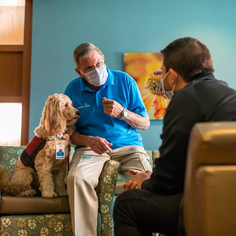 An AdventHealth employee with a service dog and talking to a patient