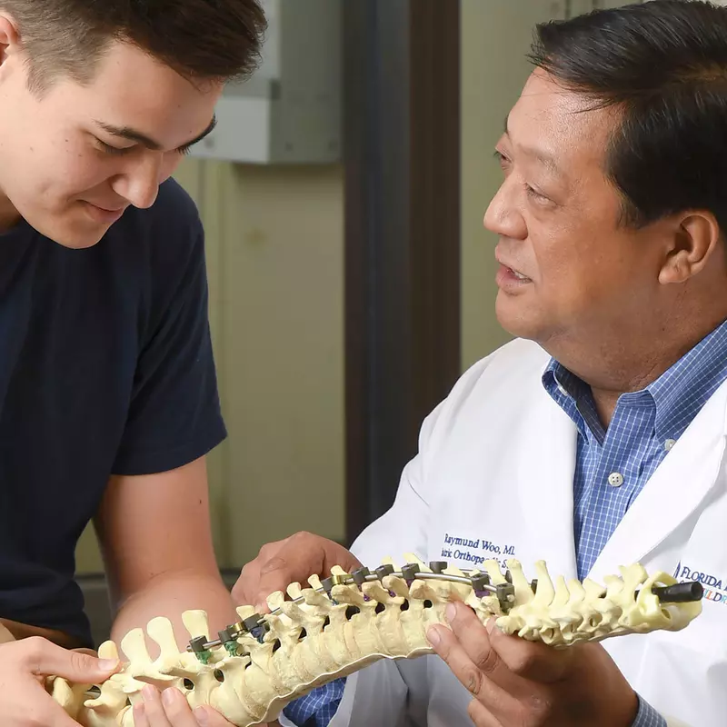 AdventHealth doctor, Raymond Woo, showing a young man a figure of a spine.