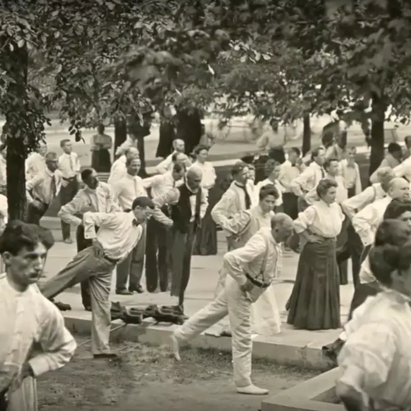 Old photograph of people balancing on one leg and stretching outdoors. 
